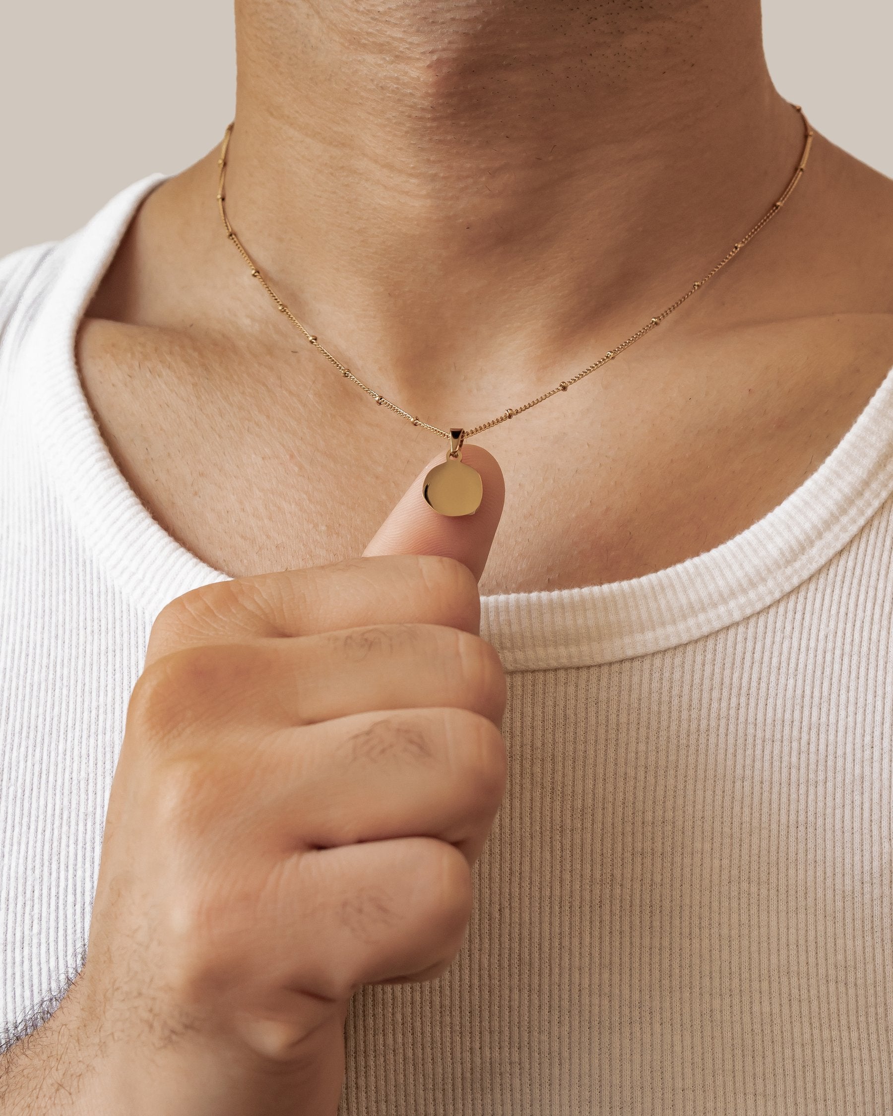 Man wearing a gold ball chain necklace with a round pendant